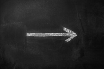 White arrow hand painted with chalk on a black blackboard indicating the direction