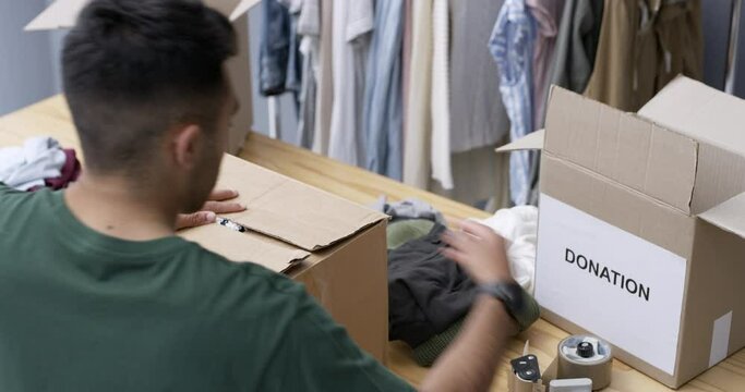 Man, seal and clothes in boxes for donation, charity and volunteer by working in organisation. Person, packing and sorting in support for community outreach, service and generosity to ngo foundation