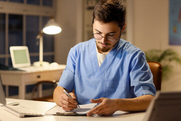 Male nurse with clipboard working evening shift at table in clinic