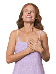 Redhead mid-aged Caucasian woman in studio laughing keeping hands on heart, concept of happiness.