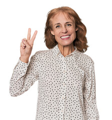 Redhead mid-aged Caucasian woman in studio joyful and carefree showing a peace symbol with fingers.