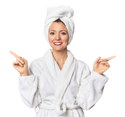 Caucasian woman in bathrobe and towel pointing to different copy spaces, choosing one of them,...