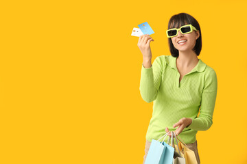 Beautiful young woman with credit cards and shopping bags on yellow background