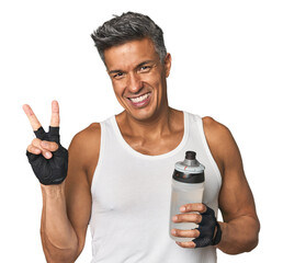 Gym-ready Hispanic man with water bottle joyful and carefree showing a peace symbol with fingers.