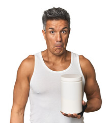 Middle-aged man with gym attire and protein shrugs shoulders and open eyes confused.