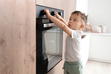 Little boy opening electric oven in kitchen. Child at risk