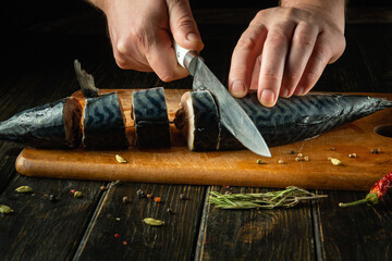 Chef preparing fresh mackerel on the kitchen table. Low key concept for preparing a fish dish. Slicing Scomber fish with a knife