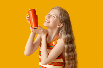 Happy young woman with can of soda on yellow background