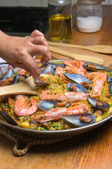 Hand gently stirring a seafood paella with shrimp and mussels using a wooden spatula, typical...