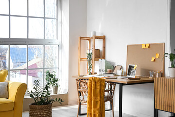 Comfortable workplace with laptop, chair and board with sticky notes in light office