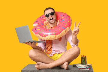 Happy office worker in sunglasses with inflatable ring and laptop sitting on table and showing...