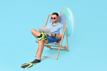 Young office worker in flippers with inflatable ring and laptop sitting on chaise lounge against...