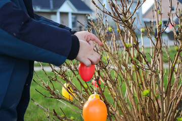 Close up of a child hanging colorful decorative easter eggs on a small bush