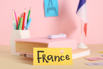Paper sheet with word FRANCE, books and stationery on table against color background