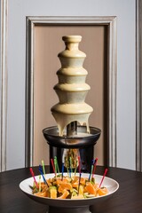 chocolate fountain made of white chocolate with pieces of fruit on sticks