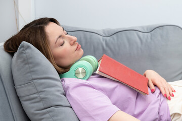 A young beautiful girl fell asleep on the sofa while reading a book	