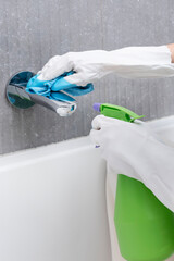 Close-up shot of woman in rubber gloves cleans sink and faucet with a rag and spray in the bathroom. Household and cleaning concept