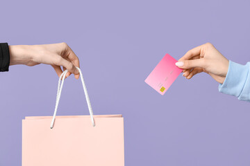 Female hands with shopping bag and credit card on lilac background