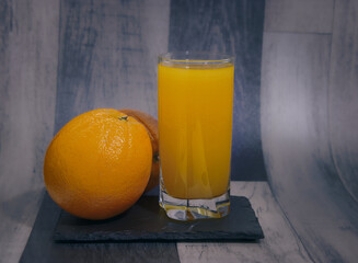 A glass of orange juice is on a table with three oranges3