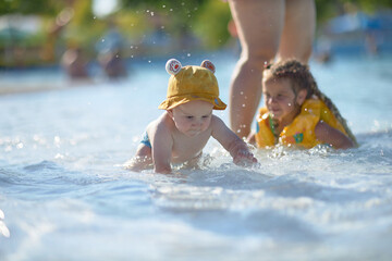 a little half a year old, a baby baby crawling on the water, smiling, outdoors, in a panama hat, in...