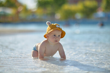 a little half a year old, a baby baby crawling on the water, smiling, outdoors, in a panama hat, in diapers, in the sun at the resort.