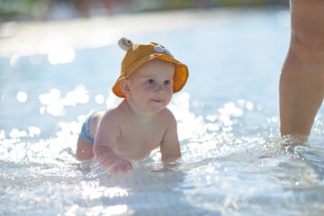 a little half a year old, a baby baby crawling on the water, smiling, outdoors, in a panama hat, in diapers, in the sun at the resort.