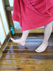 Washed feet barefoot on wooden shower tray, red terry towel, textured surface