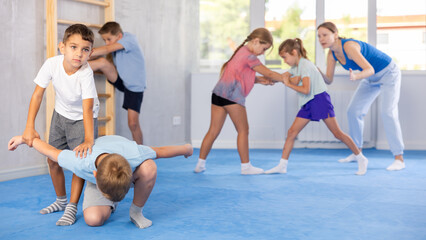 Preteen children practicing in pair self-defence movements with female trainer supervision