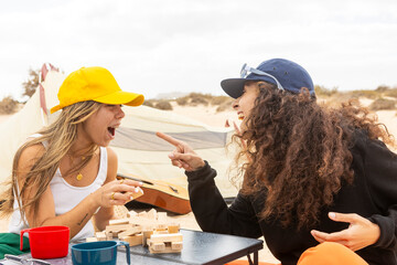Two women share a playful moment over an exciting game of blocks at their seaside campsite, exuding joy and camaraderie