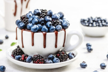 Chocolate mug cake with blueberries and blackberries in a white ceramic mug on white background