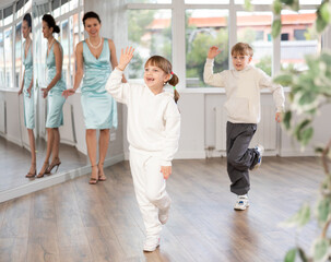 Smiling preteen girl practicing vigorous jitterbug moves with boy partner during dance lesson in choreography studio under guidance with female teacher..