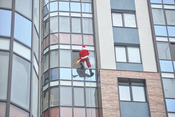 santa descends through the window of a multi-storey apartment building in order to give a gift to a child.