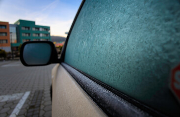Frozen side window of a car in front of a modern apartment building in a modern neighborhood,...