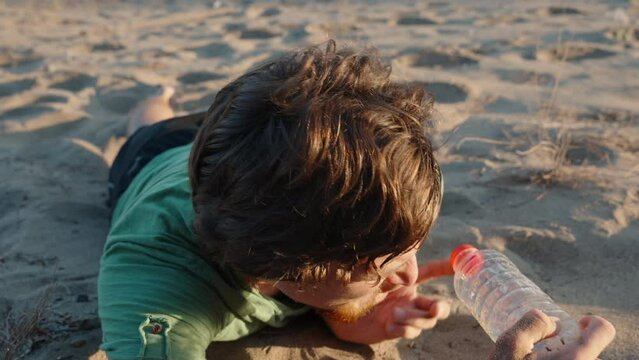 A man lies on the sand under the scorching sun in the desert. He tries to find the water in the bottle, but it's empty. He's thirsty