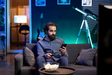 Person in home theater binging series on streaming service, texting friend on phone. Man in neon...