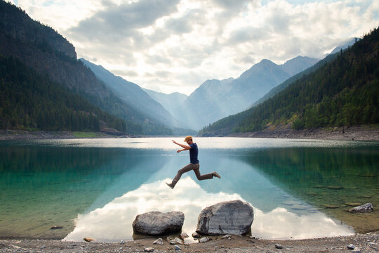 Man jumping rocks on a lake with mountains