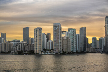 Fototapeta premium Miami, Florida, USA - July 29, 2023: Gray to yellow colored sky over buildings on Brickell Key island at evening 19:47. Centinel statue between Tequesta points. River mouth on right 