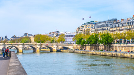 A view of the tranquil Pont Neuf over the Seine with pedestrians enjoying the riverside scene. Paris, France