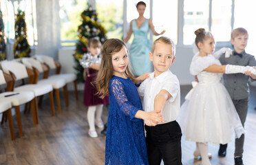 Positive elementary students in festive attire rehearsing ballroom dance number for upcoming...