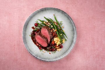 Traditionell gebratenes Rehrückenfilet mit Spätzle, Bohnen Pinienkerne in Wildsauce serviert als Draufsicht auf einem Nordic Design Teller  © HLPhoto
