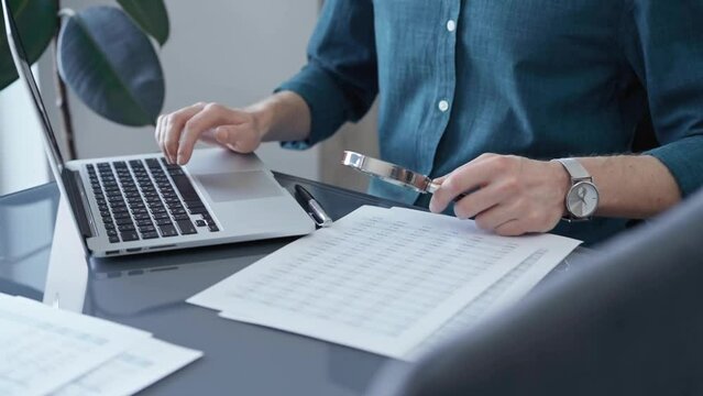 Businessman or professional auditor is analyzing data sheets. Auditing financial documents with magnifying glass and laptop. Finance audit and business
