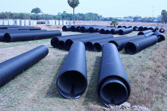 Plastic corrugated drainage pipe. Many large black HDPE plastic pipes for installing wastewater and water supply systems are piled up on the lawn at a construction site with copy space with selective 