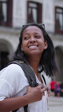 Vertical video of a smiling young African-American woman walks through a city square. A beautiful tourist happy as she looks around and admires the architecture of the European city