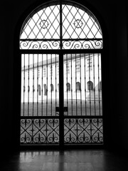 Black and white image of an ornate iron gate with a view of a courtyard through its patterned design.