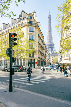 Pedestrians walk near a street corner with the Eiffel Tower in the background on a clear day. Paris, France