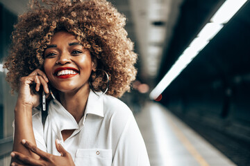 Beautiful fashionable black woman standing at a subway train station. She is happy and talking to...