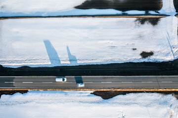 ドローン写真：夕日に照らされた広大な冬の田んぼに囲まれた道路を走る、車の影	
