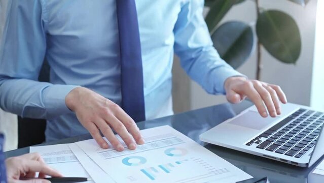 Businessman and woman analyzing data at glass desk beside a laptop in modern fair office, close up view. Business concept