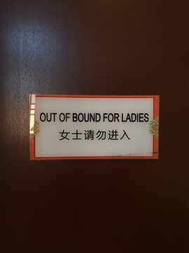 Sign reading 'OUT OF BOUND FOR LADIES' with Chinese translation on a wooden door, concept for gender restriction.
