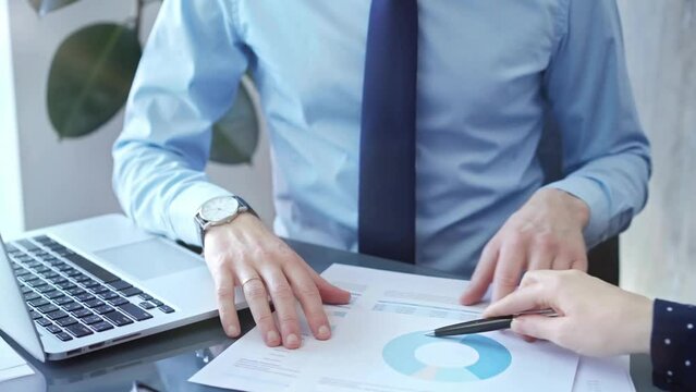 Businessman and woman analyzing data at glass desk beside a laptop in modern fair office, close up view. Business concept